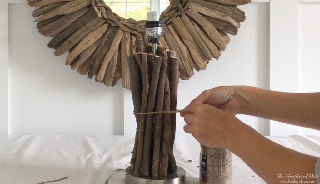 Tying jute twine around twigs arranged vertically around the base of a table top lamp