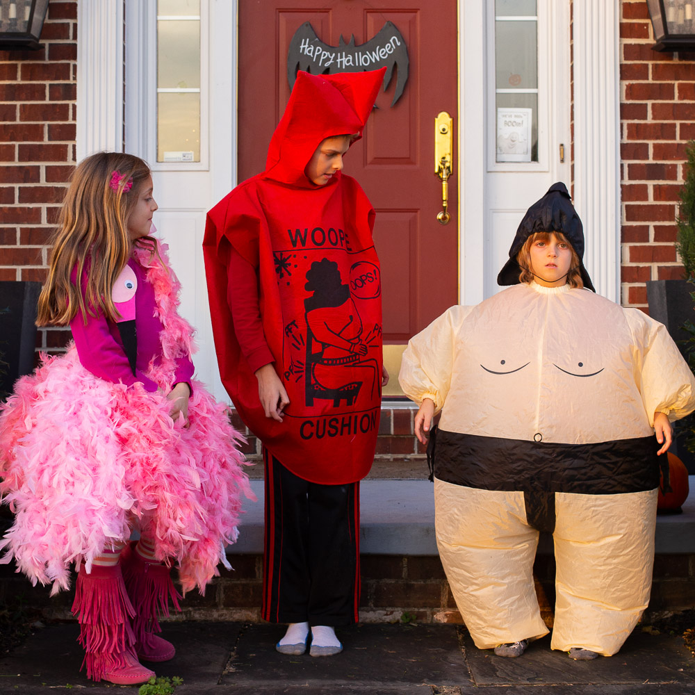 three kids in halloween costumes including a pink flamingo, whoopee cushion and inflatable sumo wrestler