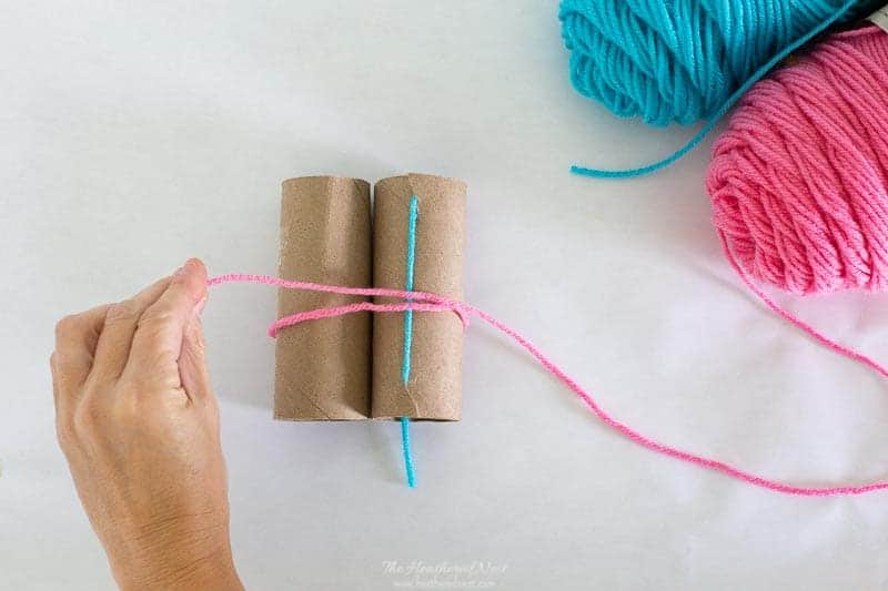 starting to loop yarn around toilet paper rolls as described in this DIY tutorial for how to make yarn pom poms.