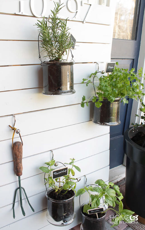 white slatted wood frame with kitchen herbs hung in clear pails with s-hooks in front of home