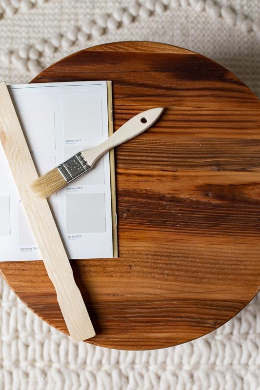 swatch of benjamin moore pale oak on a wood surface with wood paintbrush and paint stirrer