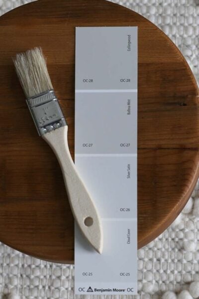 Benjamin Moore Balboa Mist OC-27 paint swatch on a wooden tray with wood paint brush