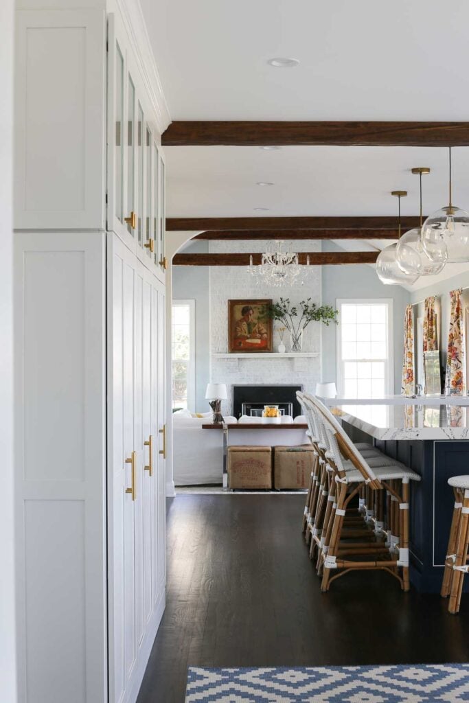 white kitchen perimeter cabinets, faux wood beams, dark hardwood floors and an open-concept kitchen/family room area in a home remodel