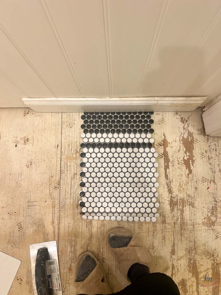 looking down at black and white penny tile samples on a bathroom subfloor