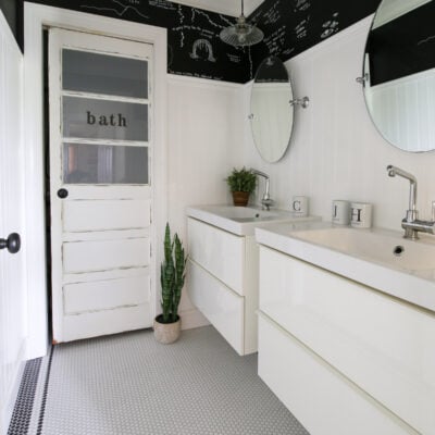 teen bathroom with black and white mosaic tile floor, black ceiling, white subway tile shower enclosure and personalized shower curtain with funny headshots of family pictures, double floating vanities, chalkboard paint walls with DIY kids chalk drawings