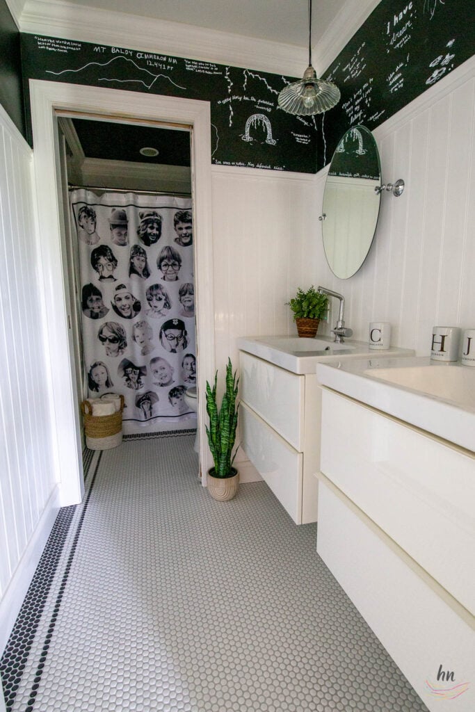 teen bathroom with black and white mosaic tile floor, black ceiling, white subway tile shower enclosure and personalized shower curtain with funny headshots of family pictures, double floating vanities, chalkboard paint walls with DIY kids chalk drawings